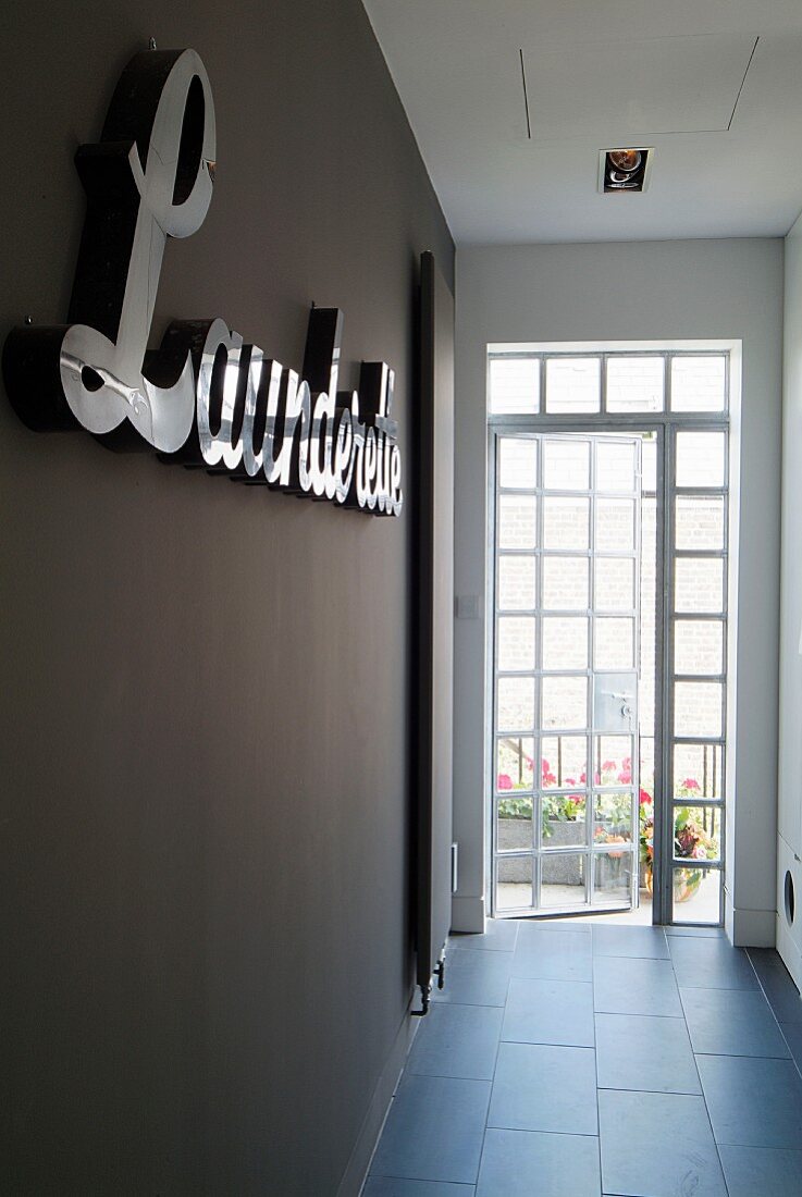 Terrace door at end of modern corridor with grey tiled floor and lettering on dark painted wall