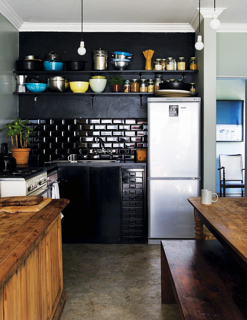 Schlichte Küchenecke in Schwarz mit Edelstahl Kühlschrankkombination und teilweise sichtbarer Holztisch mit Bank in traditionellem Ambiente