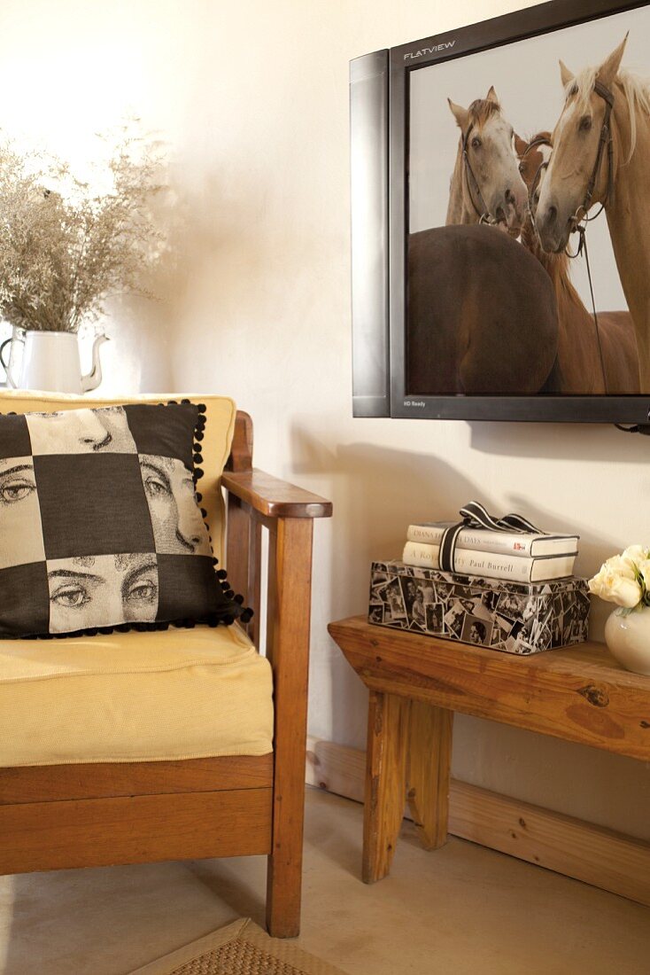 Kissen auf gelben Polstern eines Sessels mit Holzgestell neben Holzbank und Fernseher an Wand