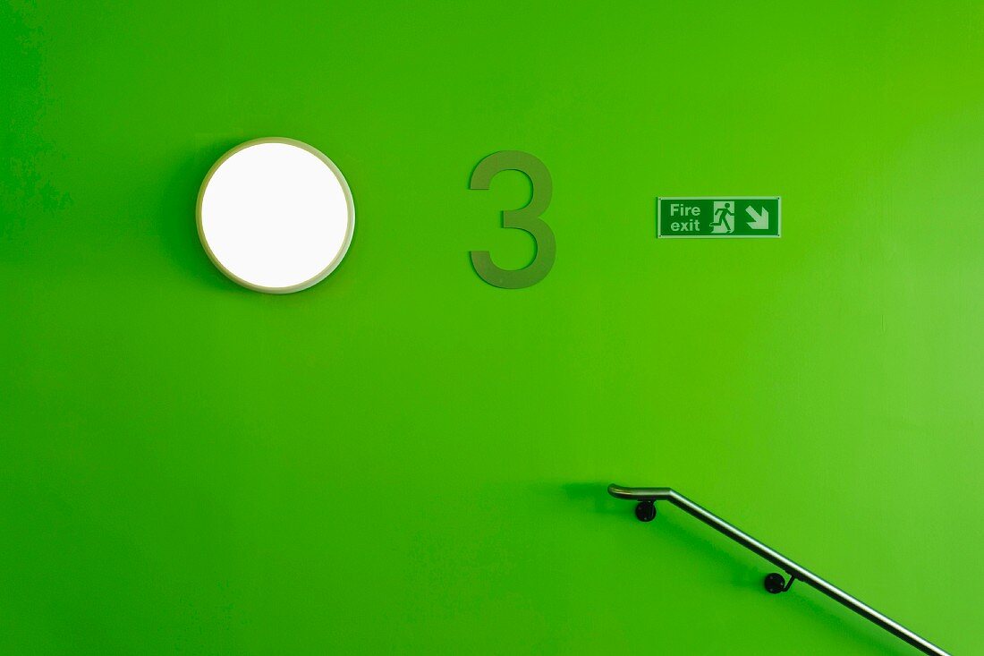 Simple, stainless steel handrail and wall lamp on green stairwell wall