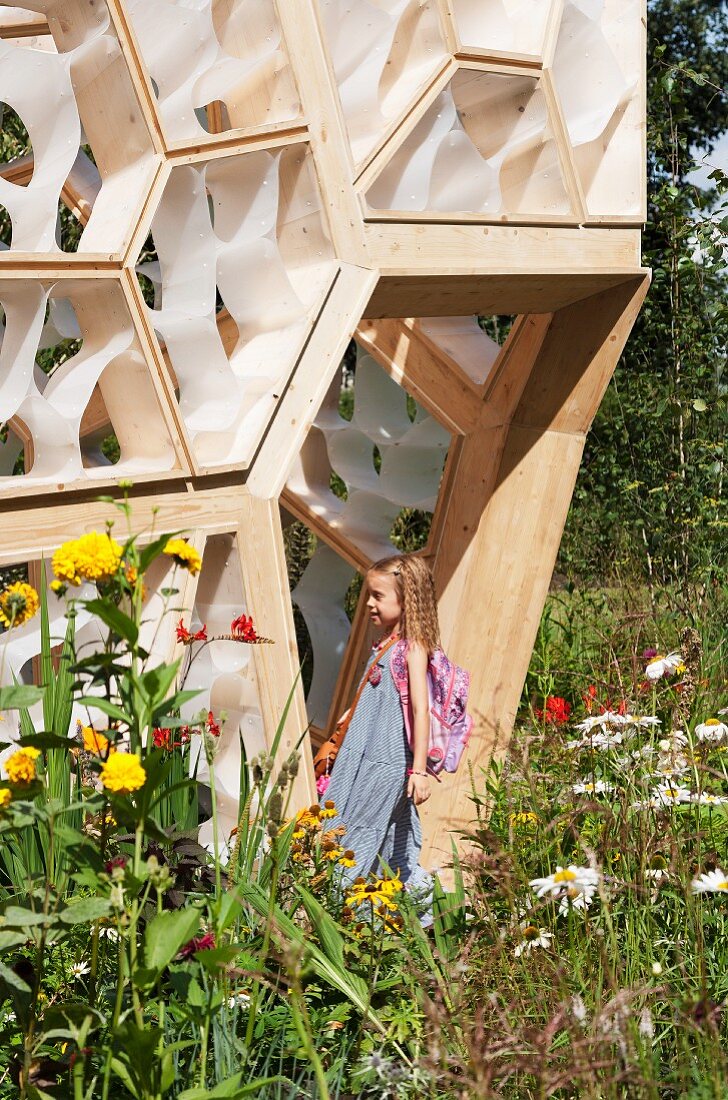 Mädchen steht in Türöffnung eines modernen Hauses mit Fassadenelementen aus Holz und Kunststoff in blühendem Garten
