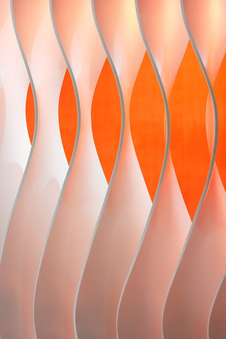 Detail eines Wandelements aus einzelnen geformten Lamellen vor orangefarbener Wand