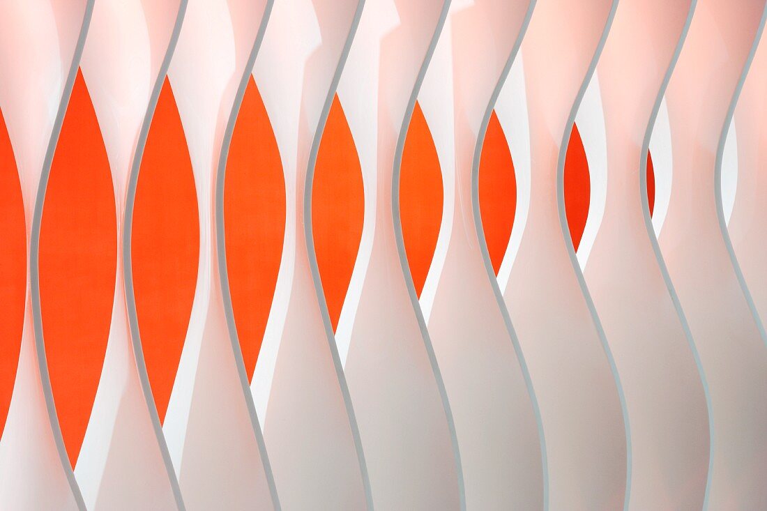 Detail of wall element made from separate, shaped blades in front of orange wall