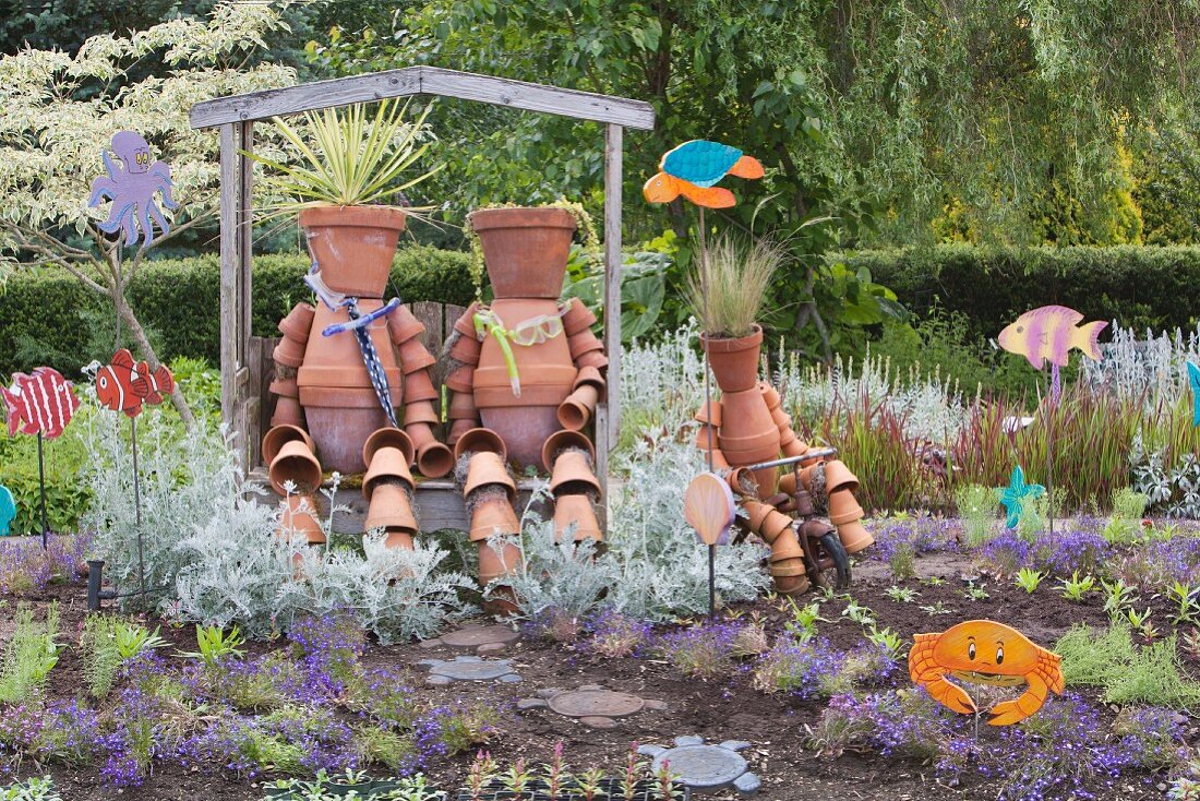 Whimsical terracotta figures made from plant pots in flowering garden