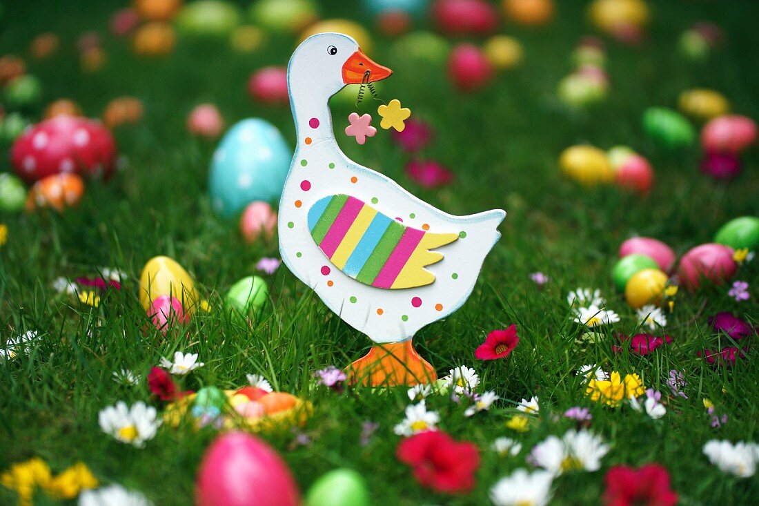 Wooden goose on lawn amongst flowers and colourful Easter eggs