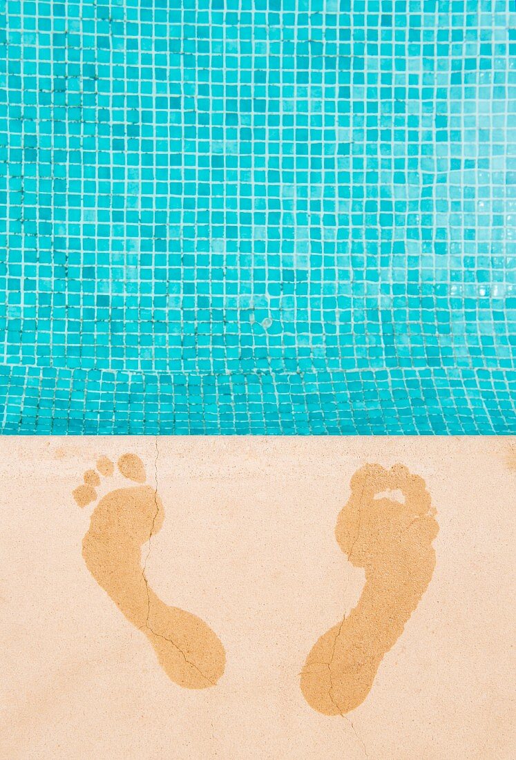 Wet footprints on surround of swimming pool with turquoise mosaic tiles