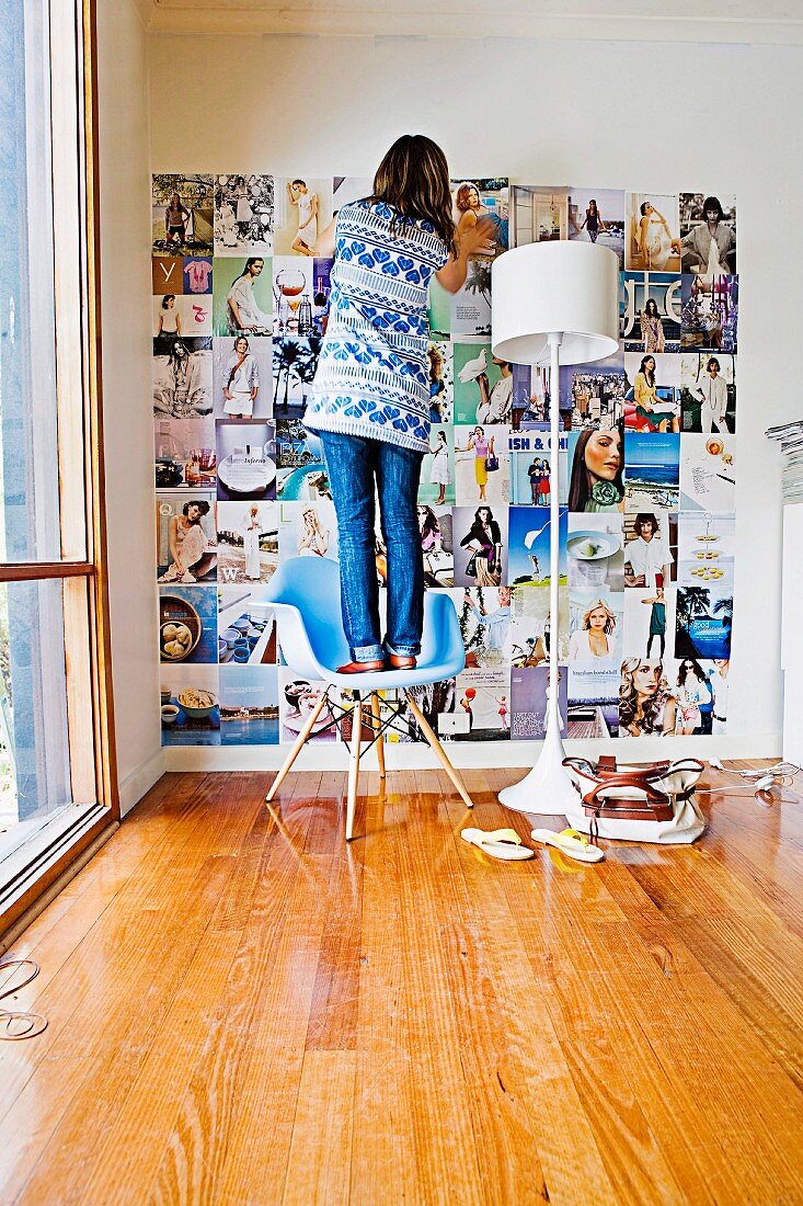 Frau, auf einem Designerstuhl stehend, klebt Fotos an die Wand