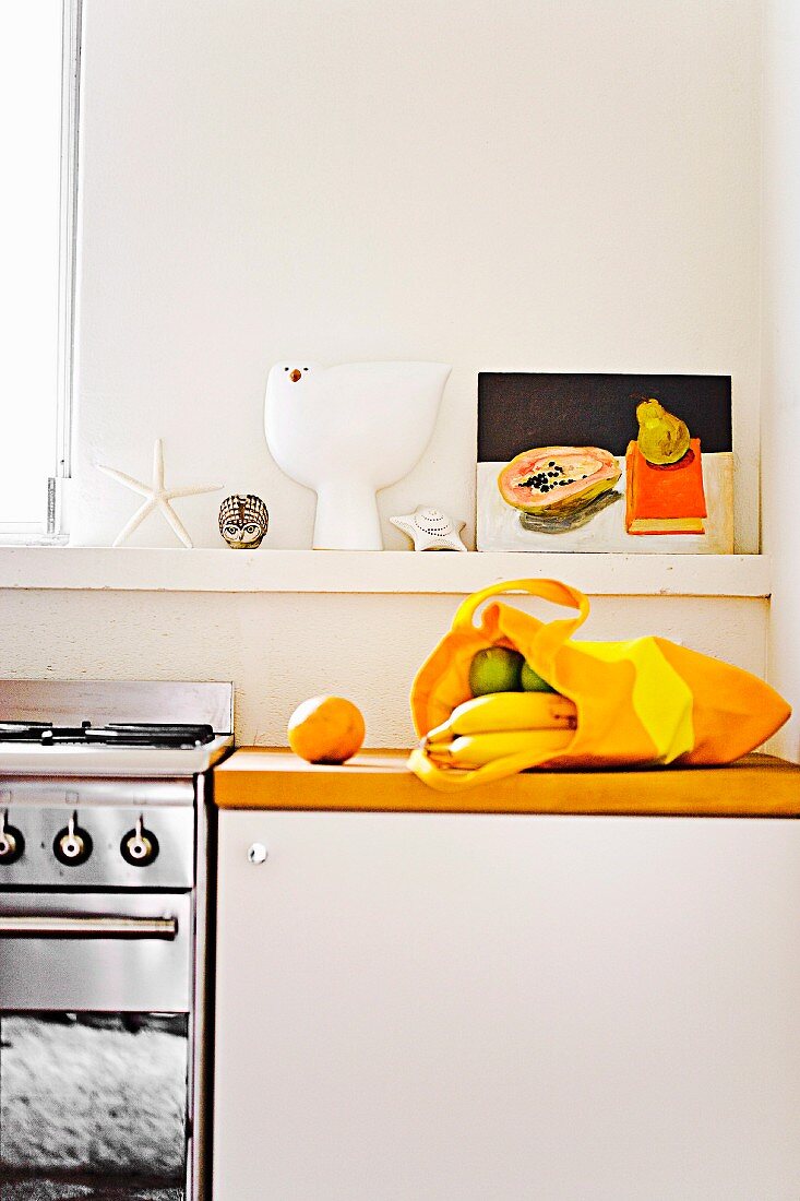 Küchenablage mit Stillleben; darunter eine gelbe Einkaufstasche mit frischem Obst