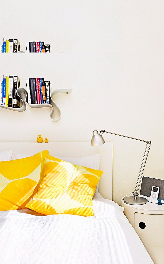 White bed with sun-yellow pillows; above it a meandering book board