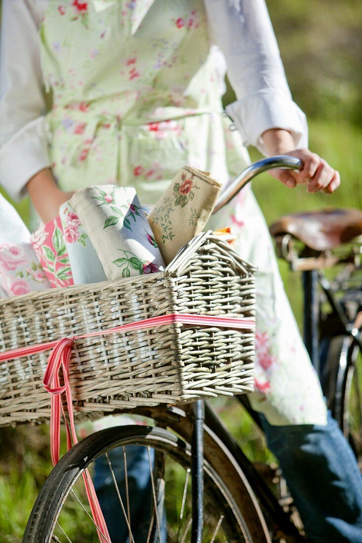 Young woman in floral apron on retro bicycle with various rose-patterned fabrics in front basket