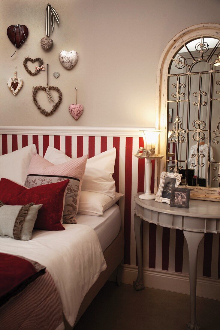 Kissenstapel auf Bett vor halbhoher, rot weiss gestreifter Holzverkleidung im Schlafzimmer