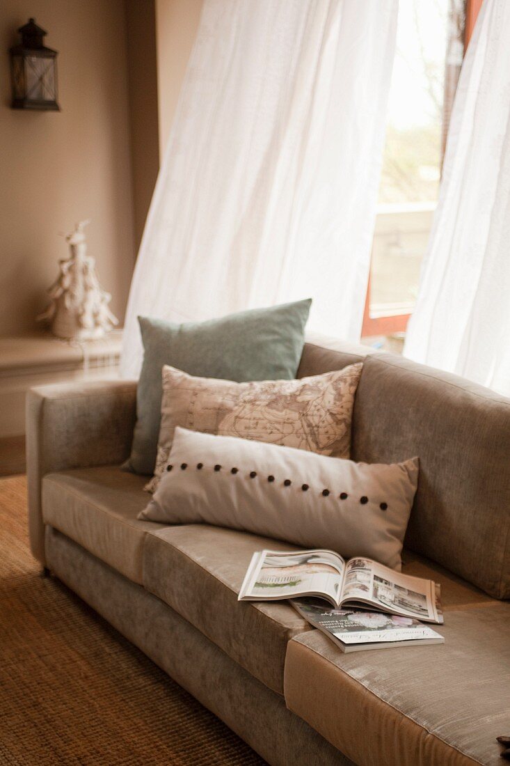 Magazines & scatter cushions on sofa in front of open terrace door