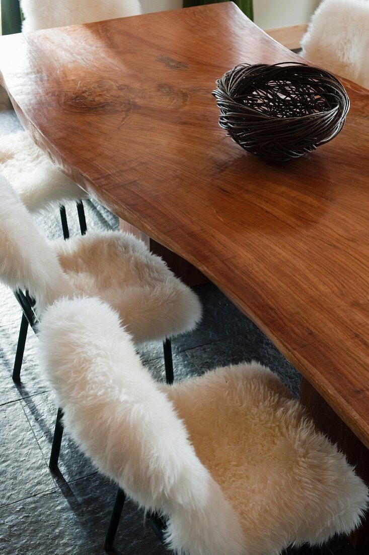 Korbschale auf polierter Tischplatte und Metallstühle mit flauschigem Lammfell
