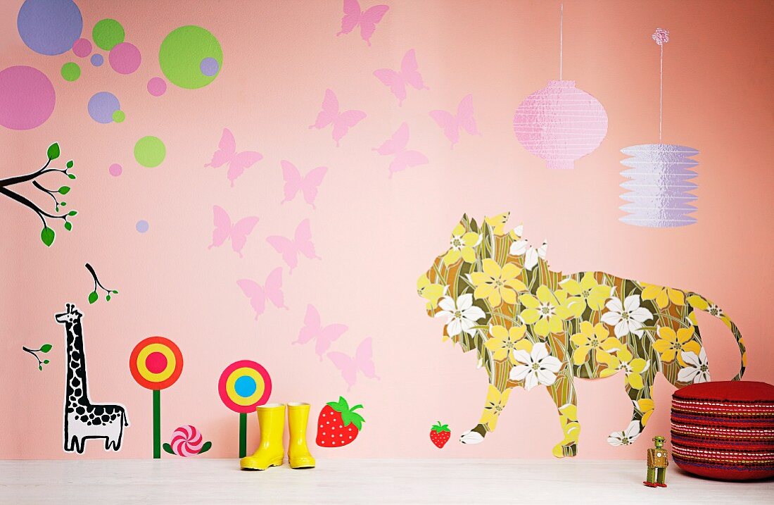 Fröhlich gestaltete Kinderzimmerwand mit blumigem Löwen, Schmetterlingen und Süssigkeiten; davor Gummistiefel und ein Polsterhocker