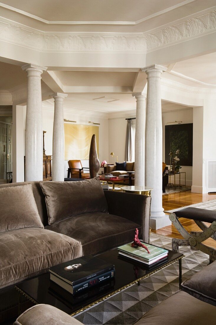 Sofa mit grauem Samtbezug und Couchtisch in Wohnzimmer vor Geviert aus Säulen unter Unterzügen mit umlaufendem Stuckfries