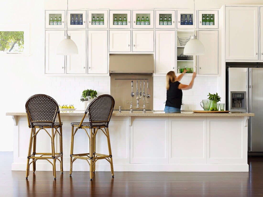 Spacious, white fitted kitchen in elegant, country-house style with bar stools at kitchen counter