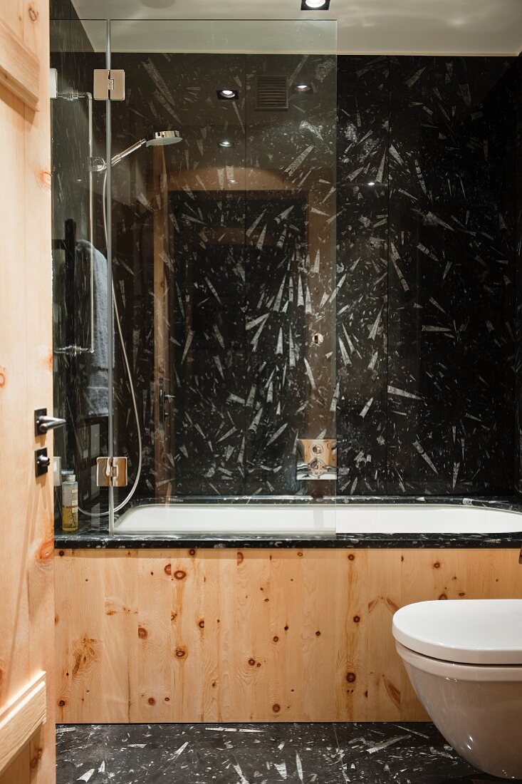 Blick in extravagantes Chalet Bad mit schwarz-weißem Naturstein an Boden und Wand und Wannenverkleidung mit Kiefernholz