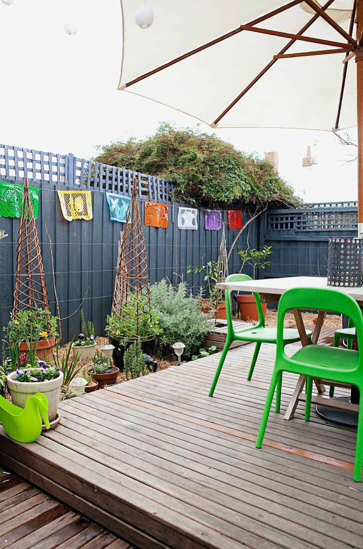 Dachterrasse mit Holzpodest, Gartenmöbeln und Sonnenschirm, vor geschmücktem Sichtschutz verschiedene Topfpflanzen