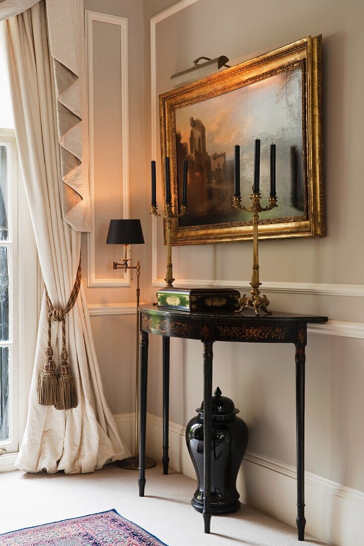 Bronze candelabras on 18th century console table and antique painting on stone grey wall; draped curtain with pelmet
