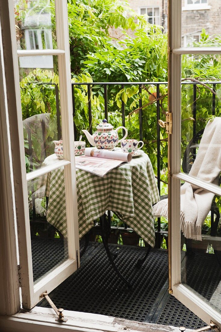 Afternoon tea on small steel balcony with climber-covered balustrade; view through open lattice window
