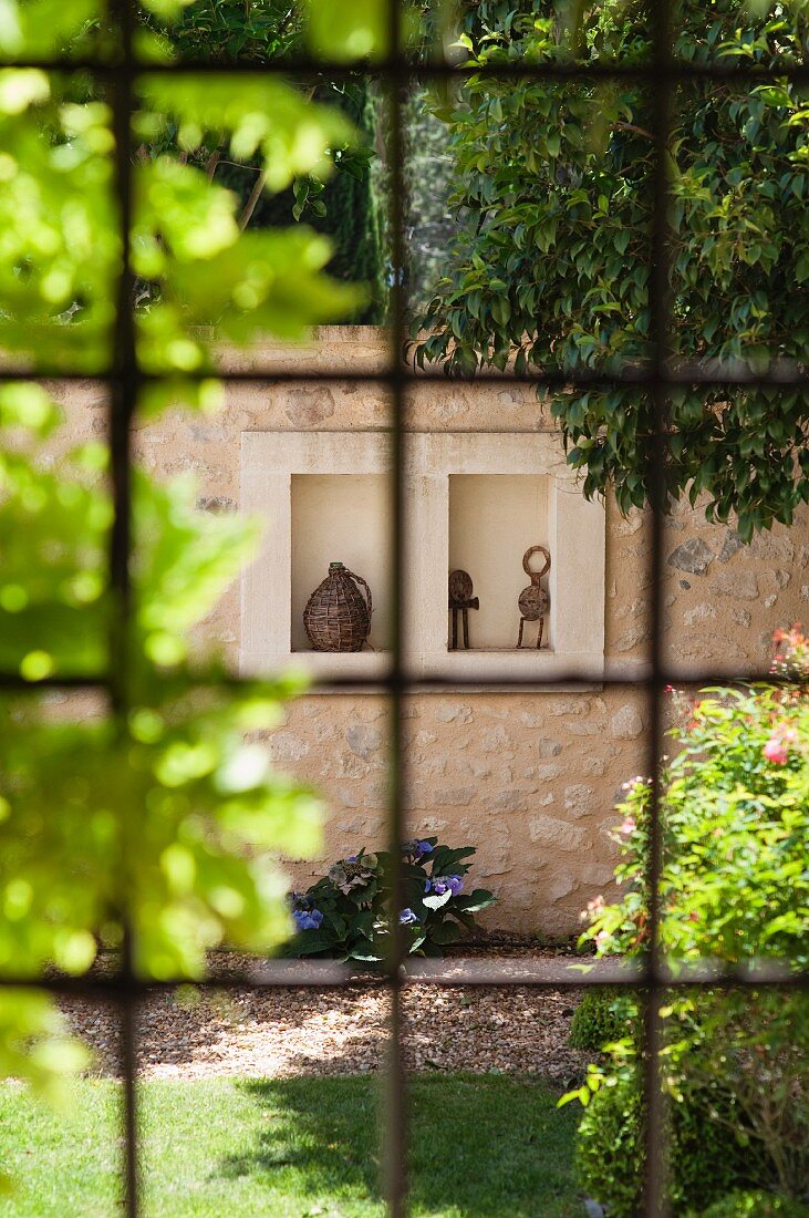 View of ornaments in niche in stone wall seen through window with original metal lattice