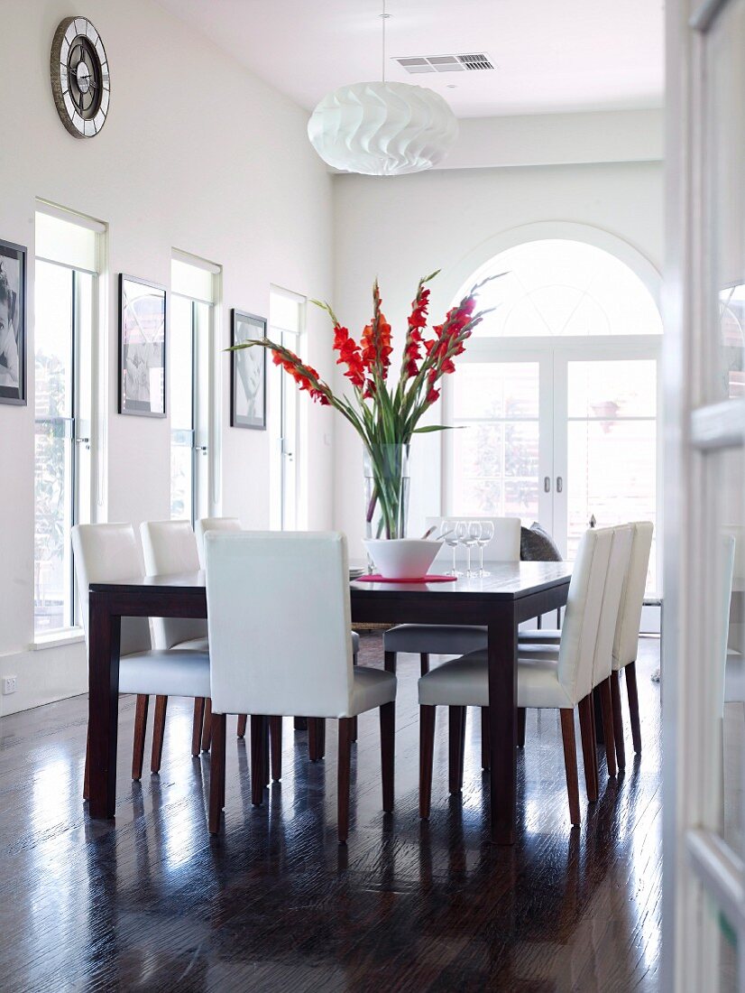 Red gladioli on large dining table and chairs with leather upholstery in classic black and white dining room