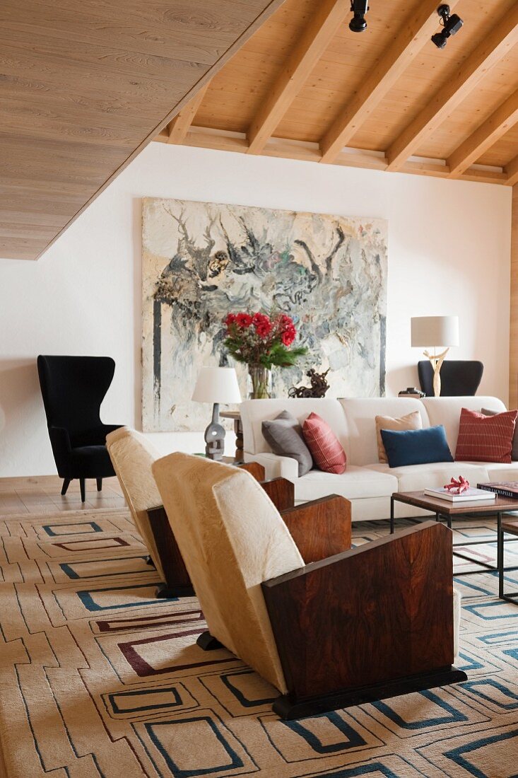 Sessel mit Holz Armlehnen und Sofa auf Teppich mit geometrischem Retromuster im Wohnzimmer mit rustikal modernem Flair
