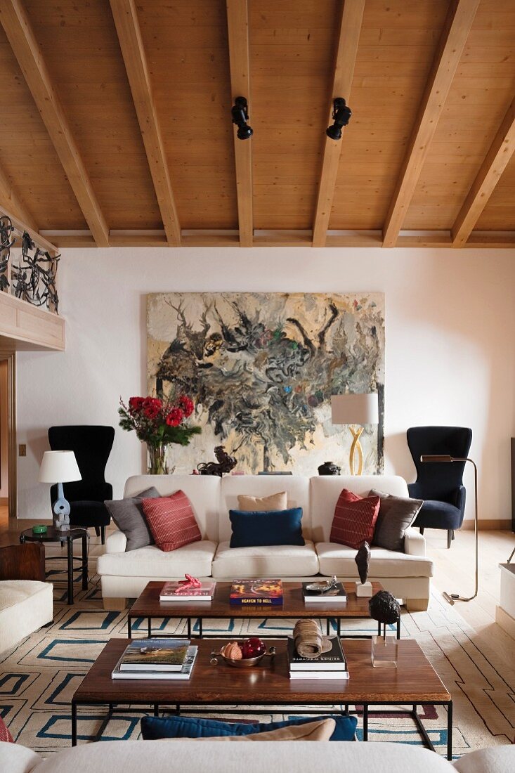 60s-style coffee tables and various scatter cushions on sofa in living room with wood-beamed ceiling