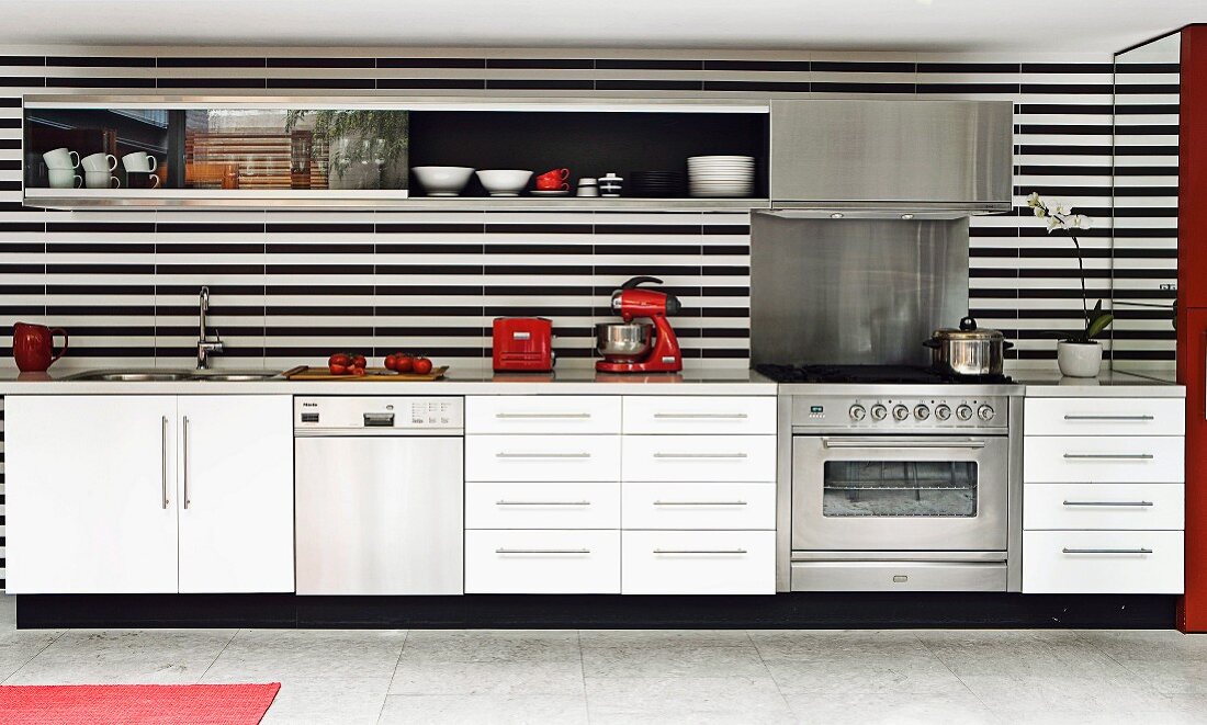 Moderne weiße Küchenzeile mit schwarz-weiß gestreifter Rückwand und seitlichem Wandspiegel und roten Küchengeräten