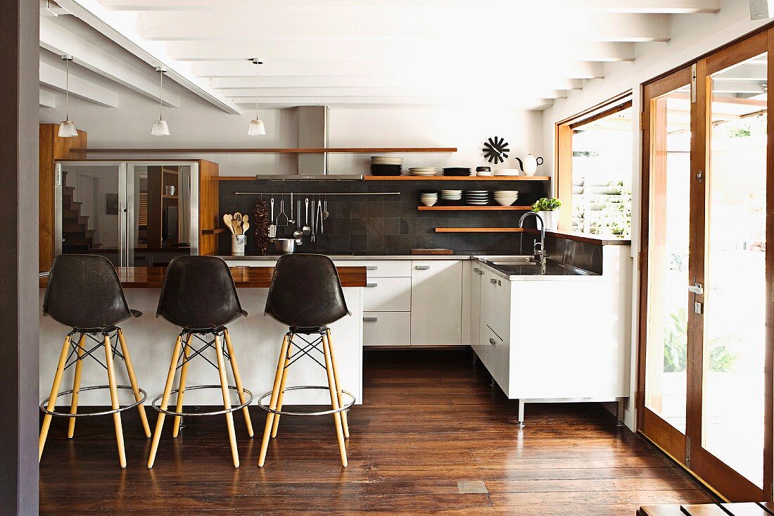Offene weiße Designerküche mit Theke, Küchenboards aus Holz und dunklem Parkettboden, seitleicher Zugang auf die Terrasse