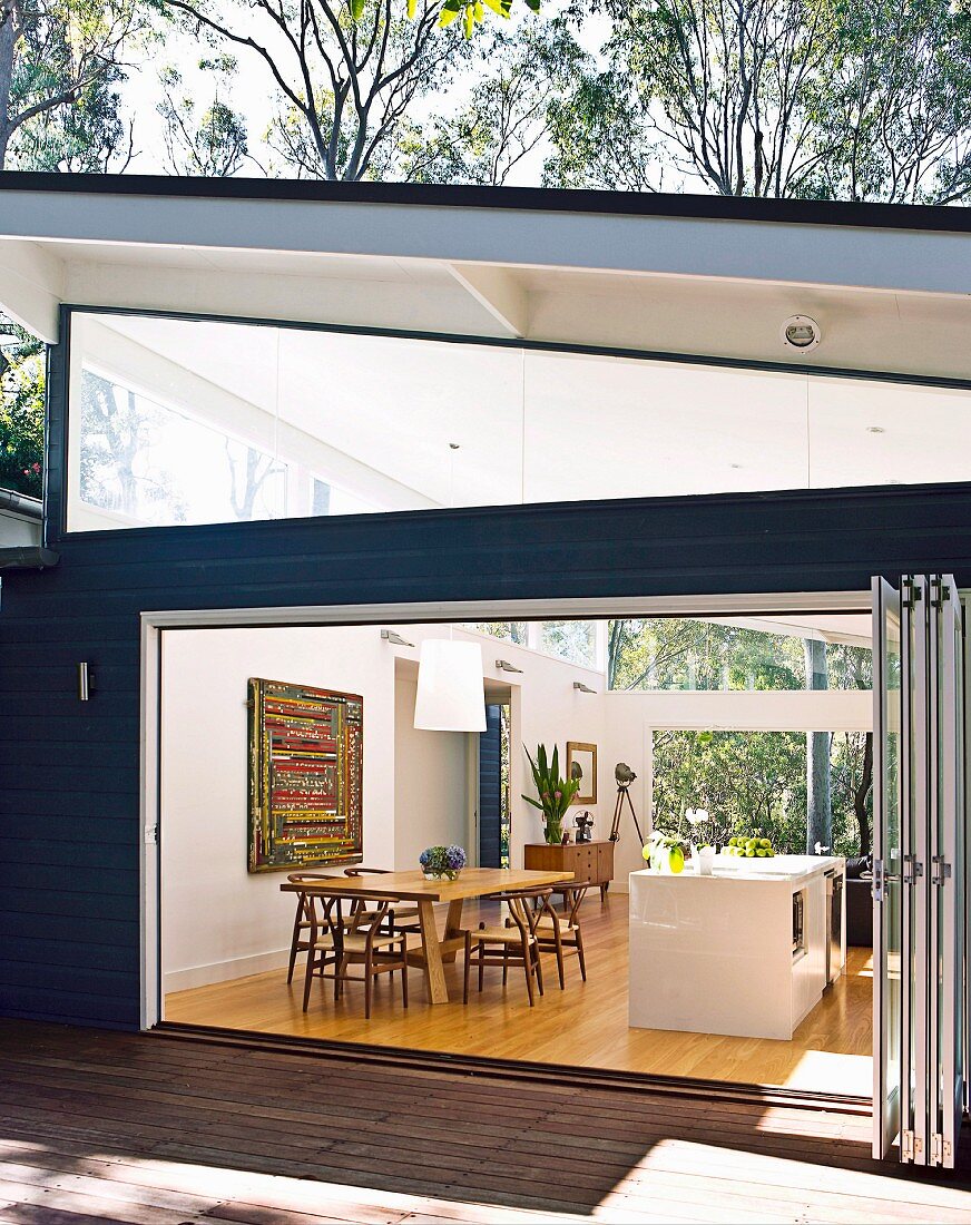 View through open folding doors of dining table and kitchen island in open-plan kitchen