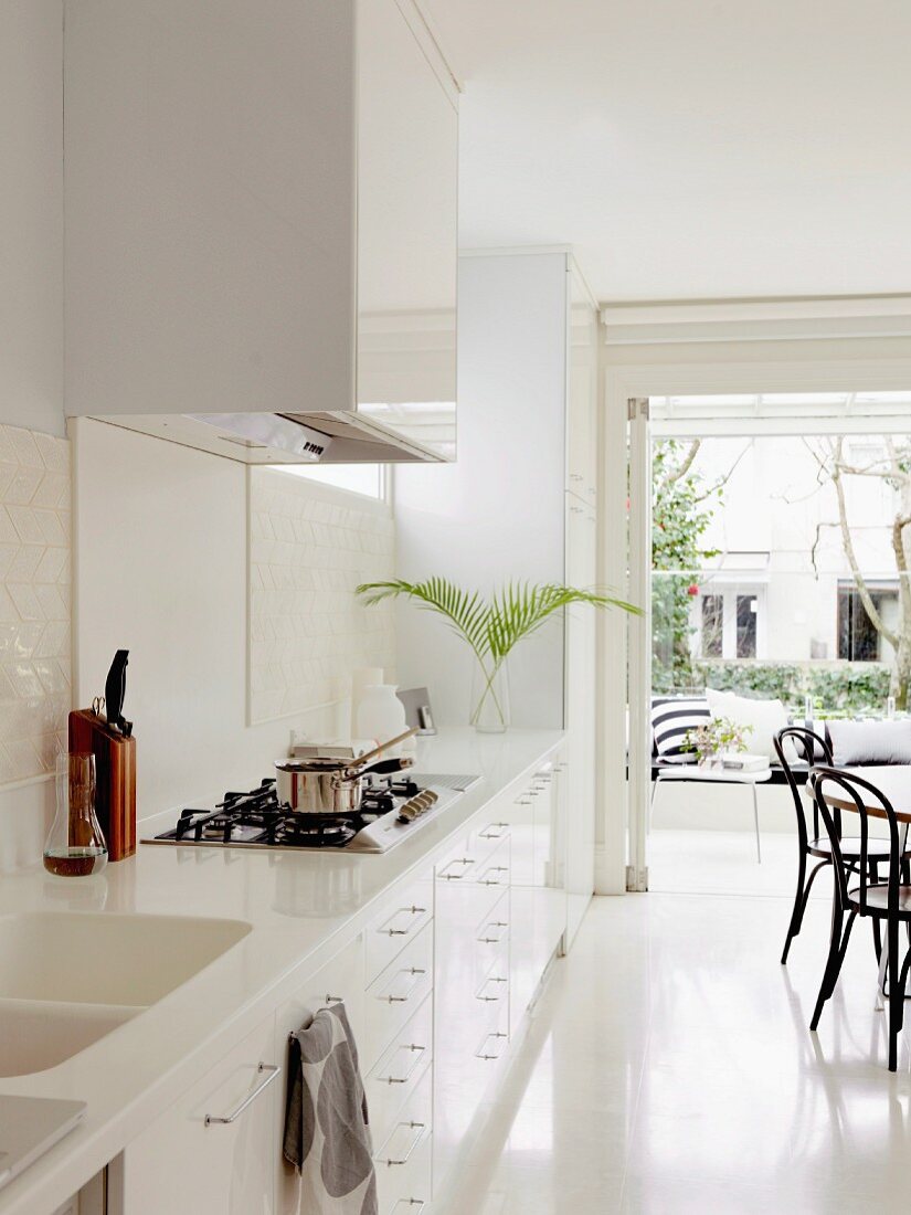 White designer kitchen with integrated sink in Corian worksurface; dining area with Thonet chairs