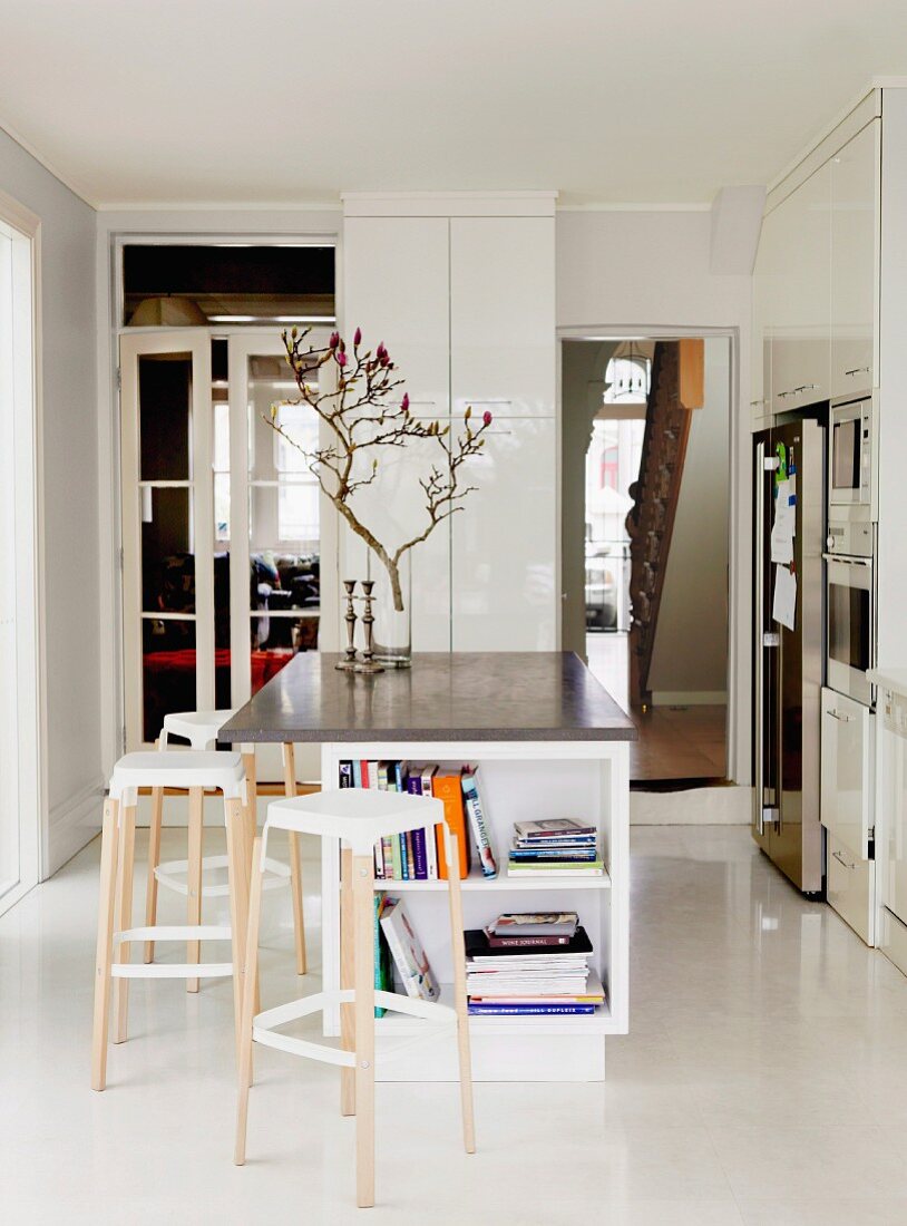 Bar stools at island counter in minimalist, white designer kitchen