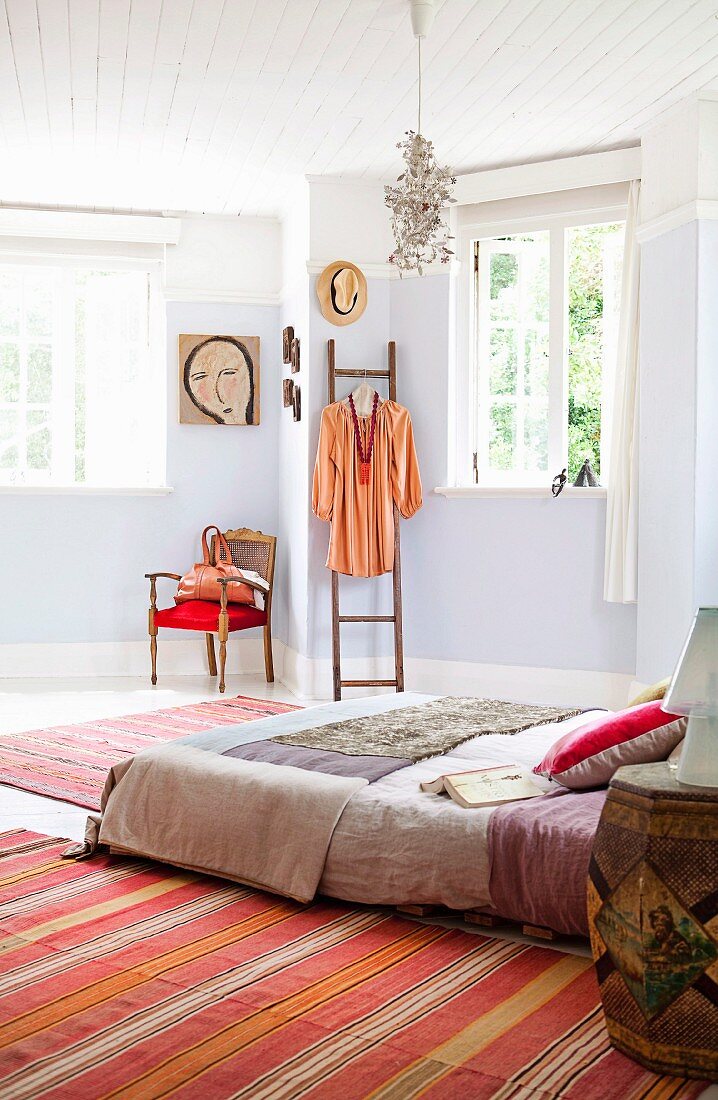 Feminine bedroom with mattress on wooden pallets, pale blue walls and dress hanging from ladder leaning on wall