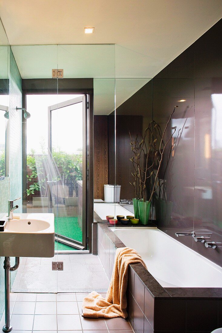 Designerbad im dunklen Braunton - Waschbecken und Badewanne vor verglastem Duschbereich mit Ausgang auf die Terrasse
