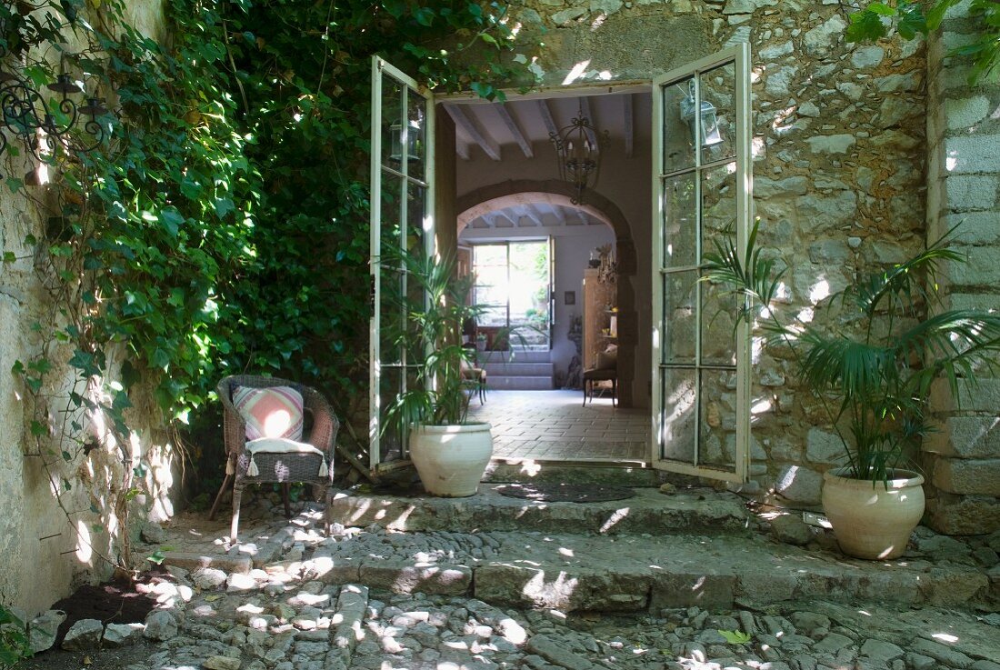 Offene Terrassentüren eines mediterranen Landhauses aus Naturstein und Blick in Wohnraum