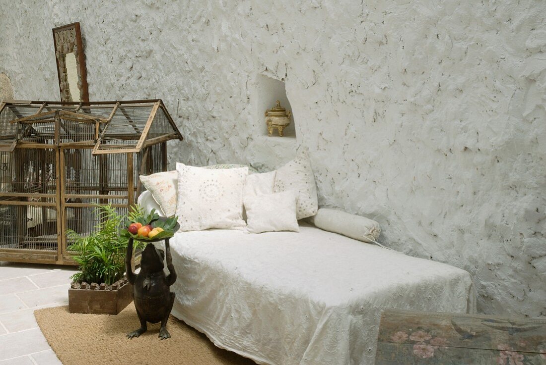 Schlichtes Tagesbett vor grossem Vogelkäfig auf Boden in Loggia eines mediterranen Wohnhauses