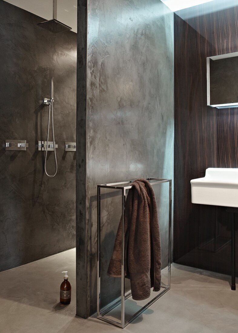 Designer bathroom with towel rail next to concrete partition separating shower area
