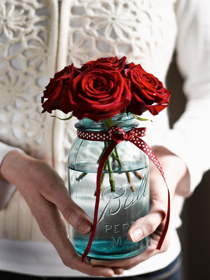 Hands holding posy of roses in preserving jar