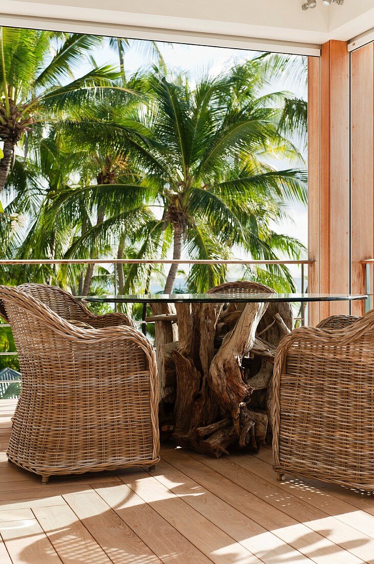 Corner of balcony with rustic table, comfortable wicker armchairs and view of palm trees