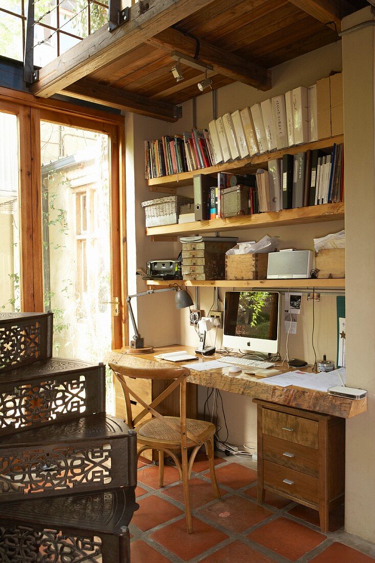 Home office with rustic desk top made from thick pine board with live edge, shelving made from scrap wood and old, artistic spiral staircase in house with many reclaimed elements