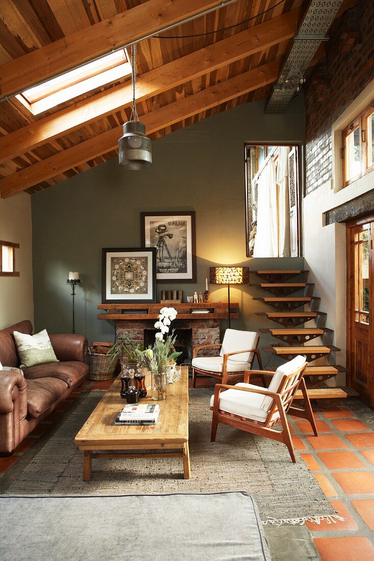 Seating area in muted colours in front of open fireplace in narrow extension with single-pitch roof; stairs with floating treads leading to outside