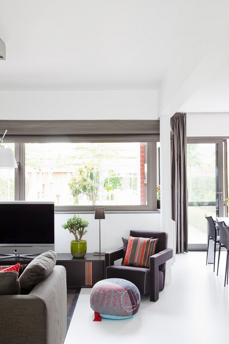 Moderner Wohnbereich mit grauer Sitzgarnitur vor Fenster und teilweise sichtbarer Essplatz