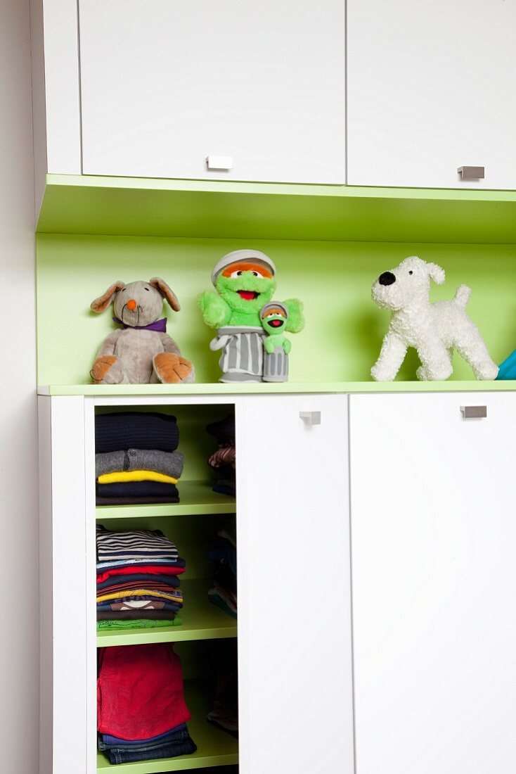 White fitted cupboards above and below green shelf in child's bedroom