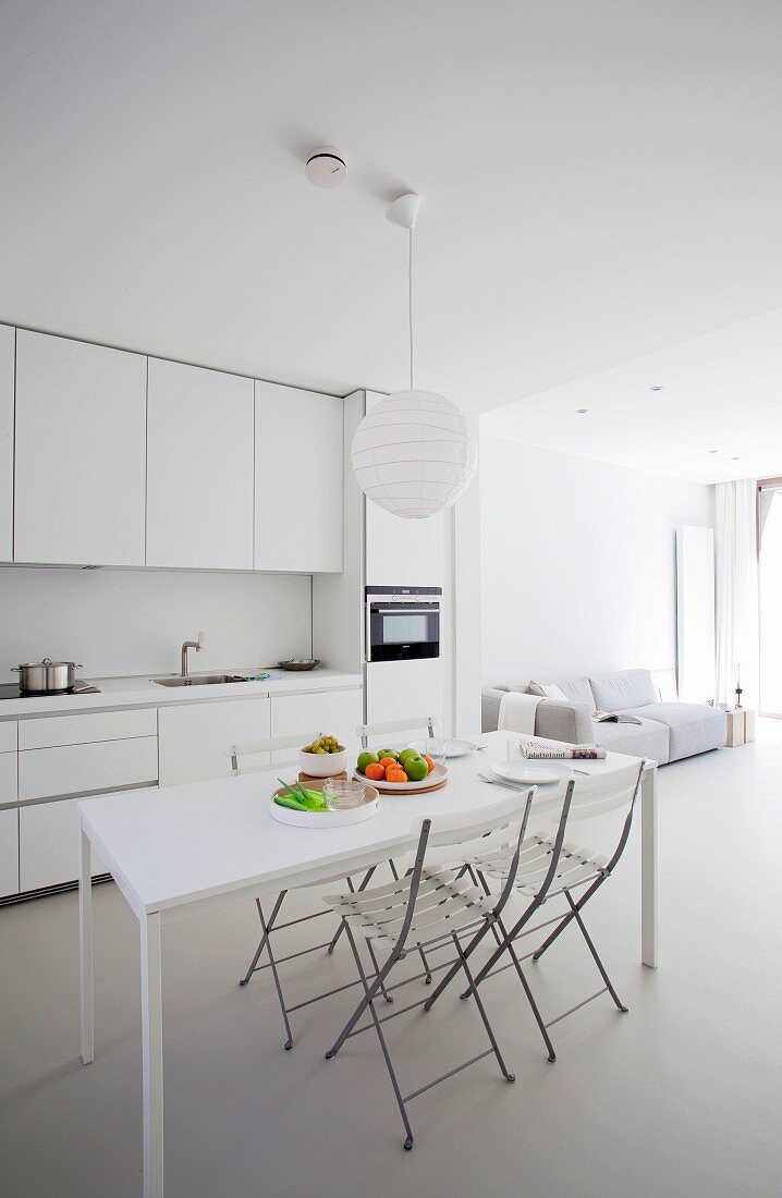 Weisser Designer Wohnraum mit Esstisch und Klappstühlen vor offener Küche