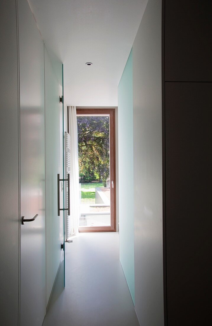 Schmaler Gang und Blick durch offene Glastür auf Gartentür in zeitgenössischer Wohnung