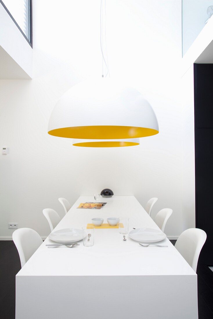 White dining area with two white, hemispherical lamps with yellow inner sides above table