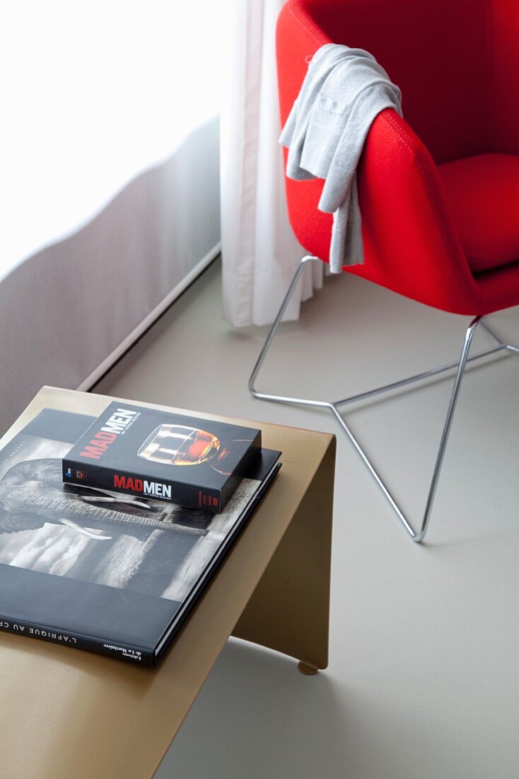 Red designer chair next to books on dimple side table