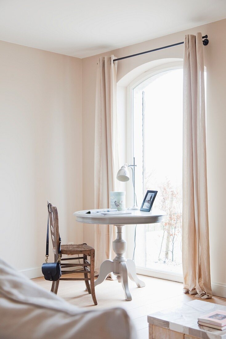 Antique, white-painted table and vintage rush-bottom chair in front of French doors in corner of bright room