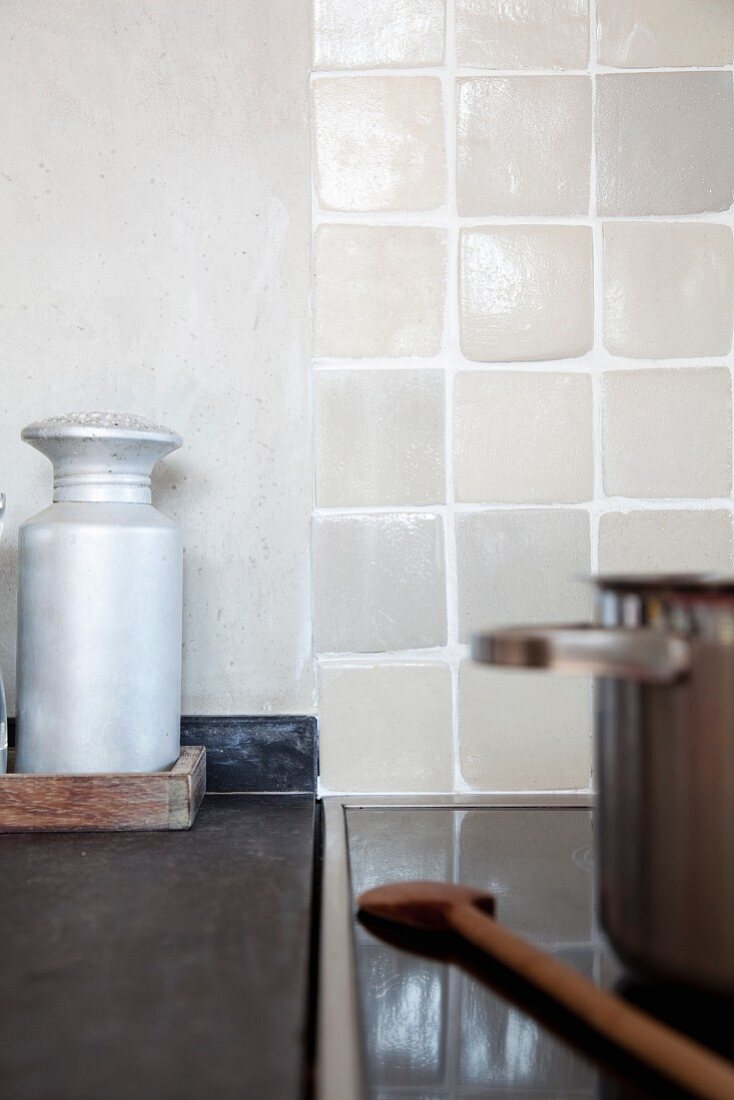 Aluminium sugar caster on grey stone surface next to pot and wooden spoon on ceran hob; splashback of pale, hand-made tiles